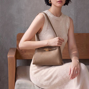SUL EXTRAS Adèle shoulder bag in taupe grained synthetic leather with gold-tone hardware held by a woman on a bench.