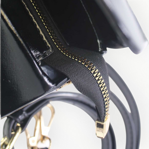 SUL EXTRAS Clarisse handbag interior view showing black patent synthetic material, gold-tone zipper, and strap details.