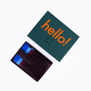 SUL EXTRAS Dudu leather card holder with blue and burgundy accents next to a green hello! branded gift box