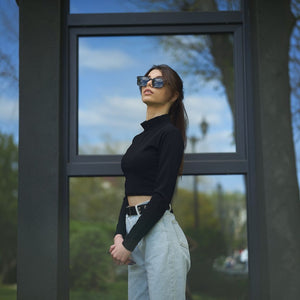 Woman wearing SUL EXTRAS Leo polarized sunglasses with black frames and dark lenses, standing outdoors.