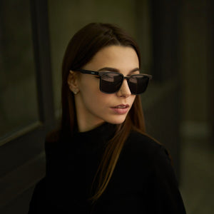 Woman wearing SUL EXTRAS Leo polarized sunglasses with black square frames and dark lenses in a stylish setting