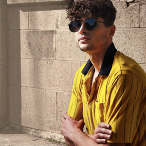 A man wearing SUL EXTRAS Parade oversized geometric round sunglasses with black frames and smoke lenses outdoors.