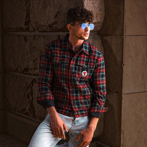 A man wearing SUL EXTRAS Parade oversized geometric round sunglasses with blue lenses, styled with a plaid shirt.