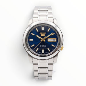 SUL EXTRAS Seiko 5 automatic watch with a midnight blue sunburst dial, gold accents, and silver stainless steel band.
