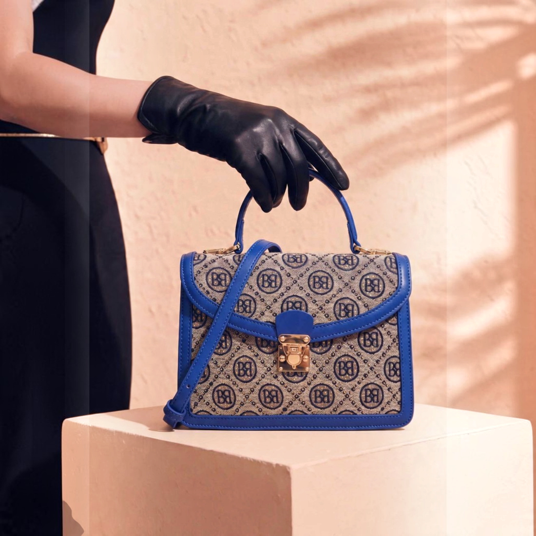 SUL EXTRAS Tom & Eva vintage monogram handbag with blue trim, gold turn-lock, and top handle held by gloved hand.