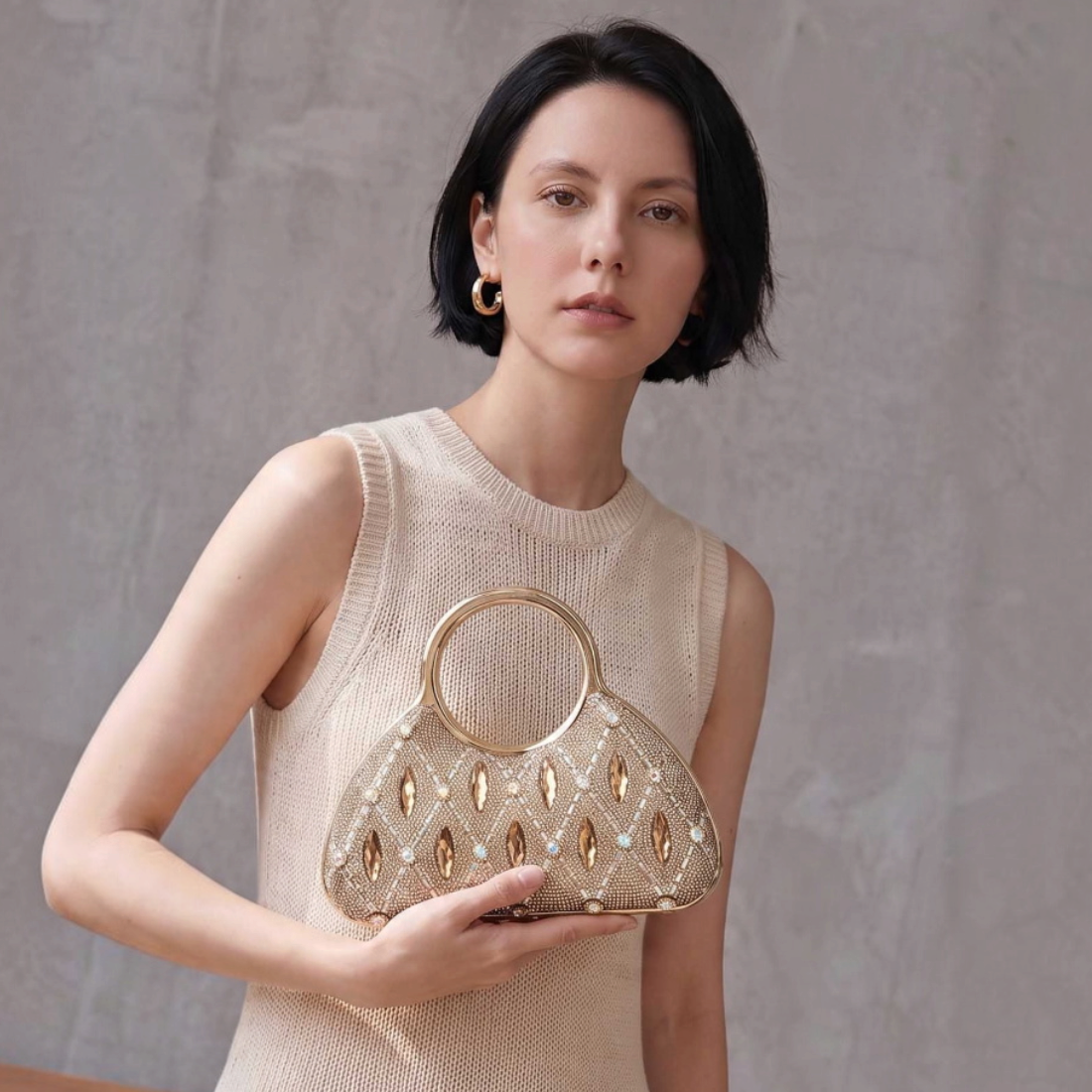 SUL EXTRAS Aurelia evening bag with gold rhinestone latticework and circular handles held by a woman in a beige dress