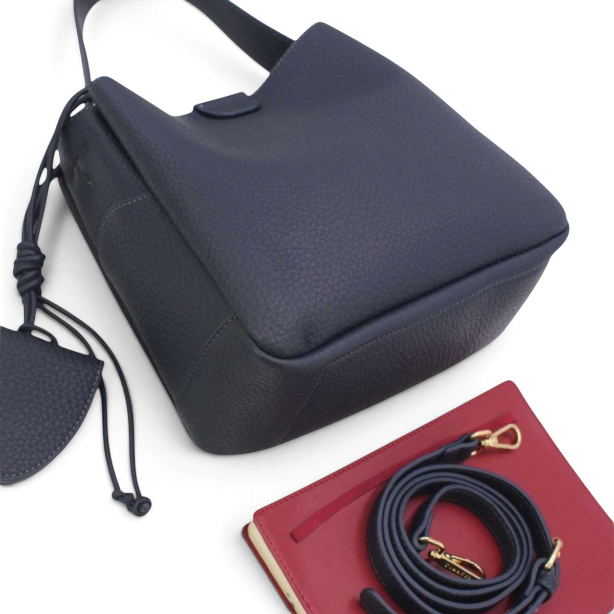 SUL EXTRAS Tom & Eva Noémie black grained bucket bag with key charm, adjustable shoulder strap, and red notebook.