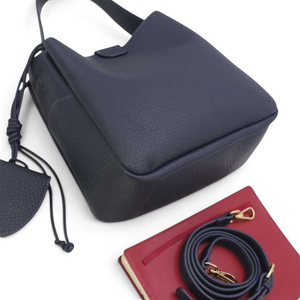 SUL EXTRAS Tom & Eva Noémie black grained bucket bag with key charm, adjustable shoulder strap, and red notebook.