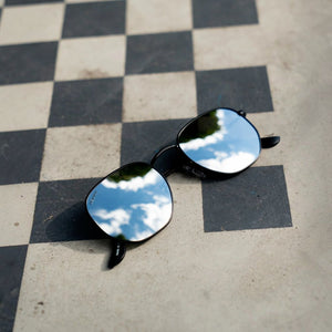 SUL EXTRAS Eternally minimalist geometric sunglasses with reflective lenses on a black and white checkered surface