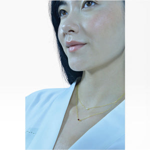 SUL EXTRAS layered gold necklace with pearl and red zirconia worn by a woman in a white top