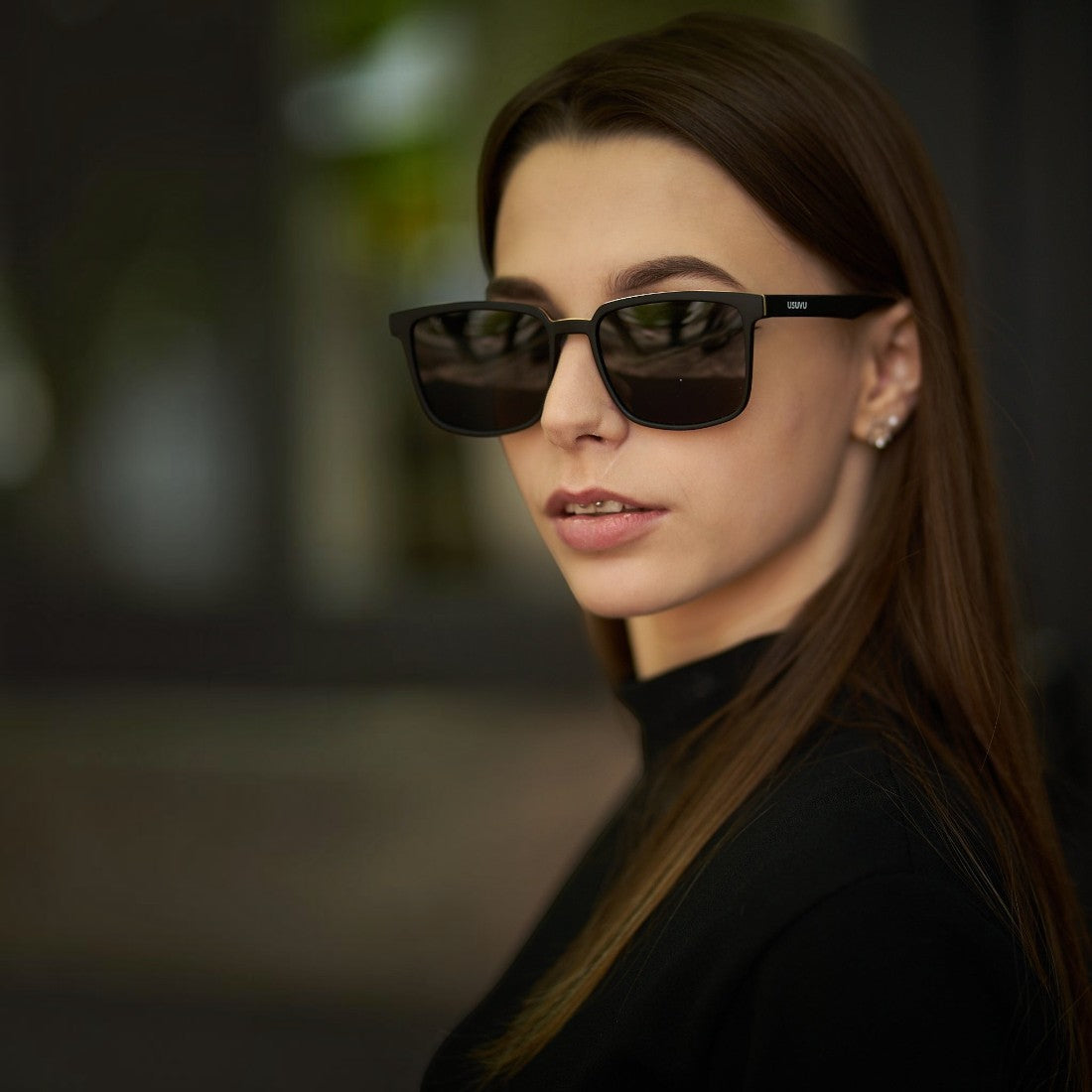 Woman wearing SUL EXTRAS Leo polarized sunglasses with a black frame and dark lenses in a stylish outdoor setting