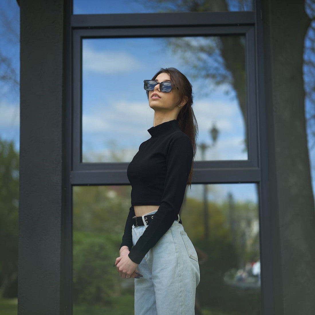Woman wearing SUL EXTRAS Leo polarized sunglasses with black frames and dark lenses, standing outdoors.