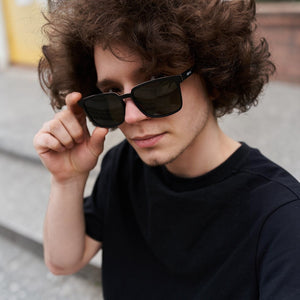 A young man with curly hair wearing SUL EXTRAS Leo polarized sunglasses with a black frame and dark lenses.