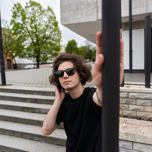 A young man wearing SUL EXTRAS Leo polarized sunglasses with a durable black frame outdoors.