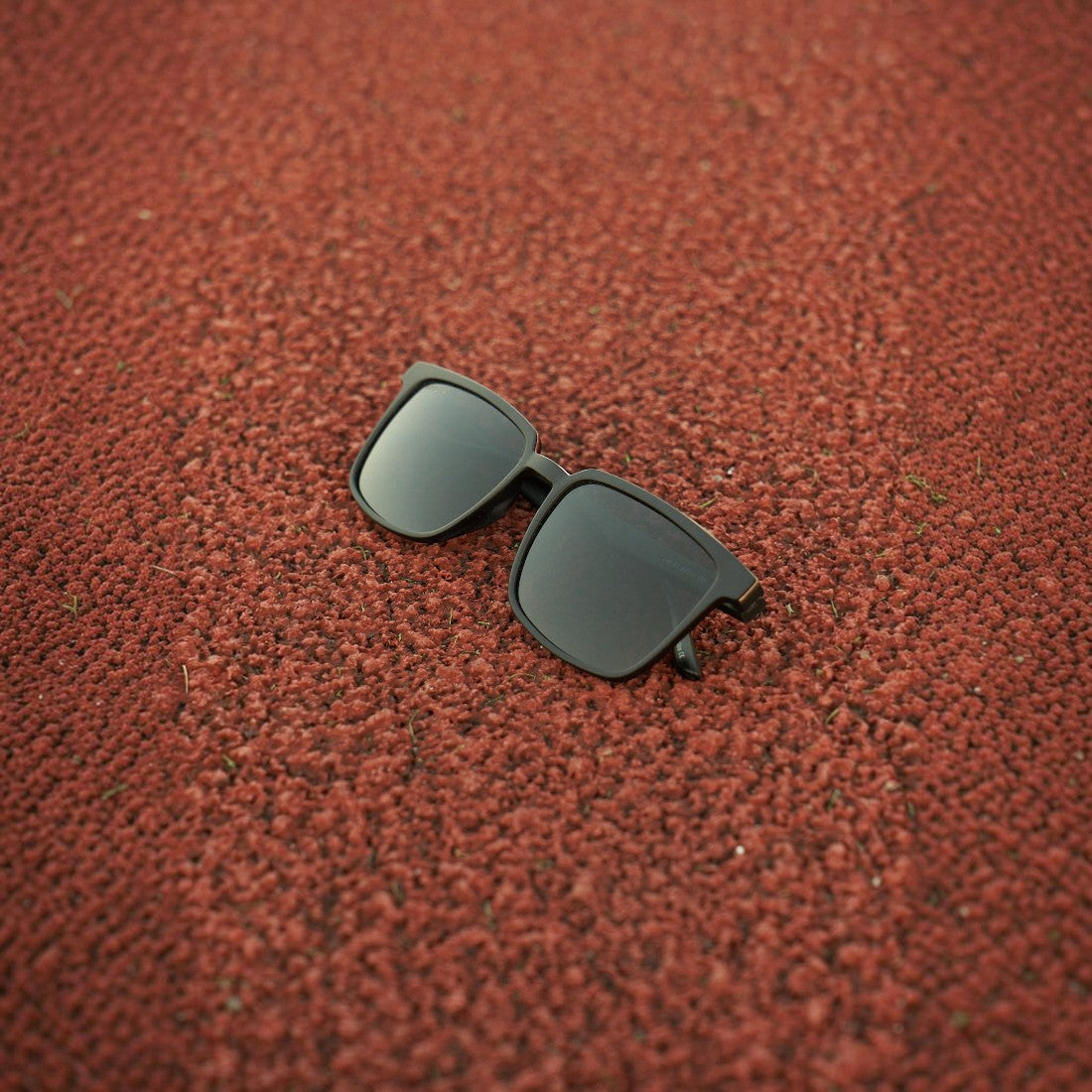 SUL EXTRAS Leo polarized sunglasses with black frames and dark lenses resting on a textured red running track surface.