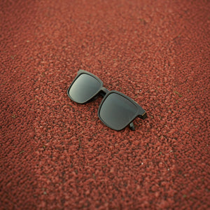 SUL EXTRAS Leo polarized sunglasses with black frames and dark lenses resting on a textured red running track surface.