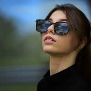 Woman wearing SUL EXTRAS Leo polarized sunglasses with black frames and dark lenses outdoors