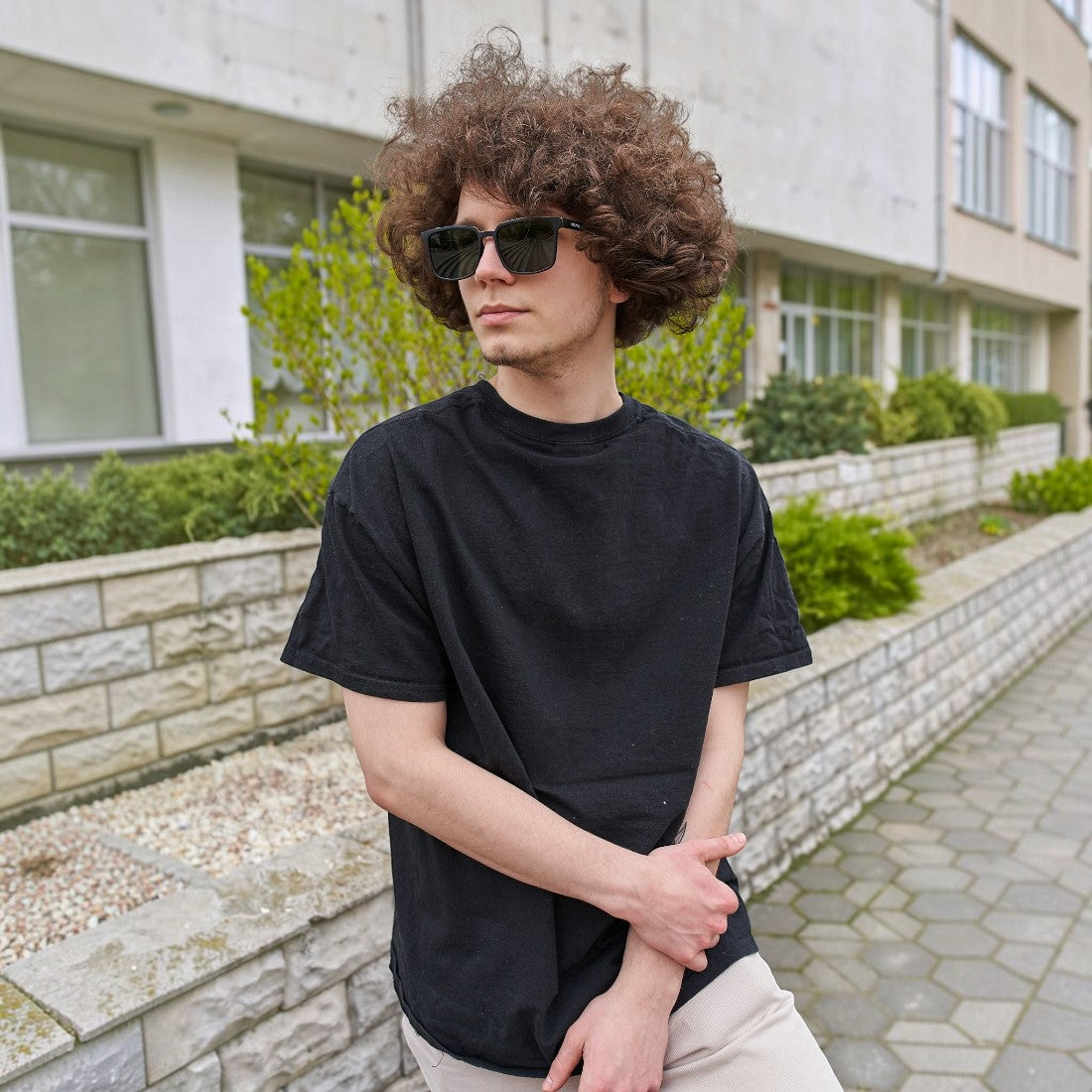 A young man with curly hair wearing SUL EXTRAS Leo polarized sunglasses with a durable black frame outdoors.