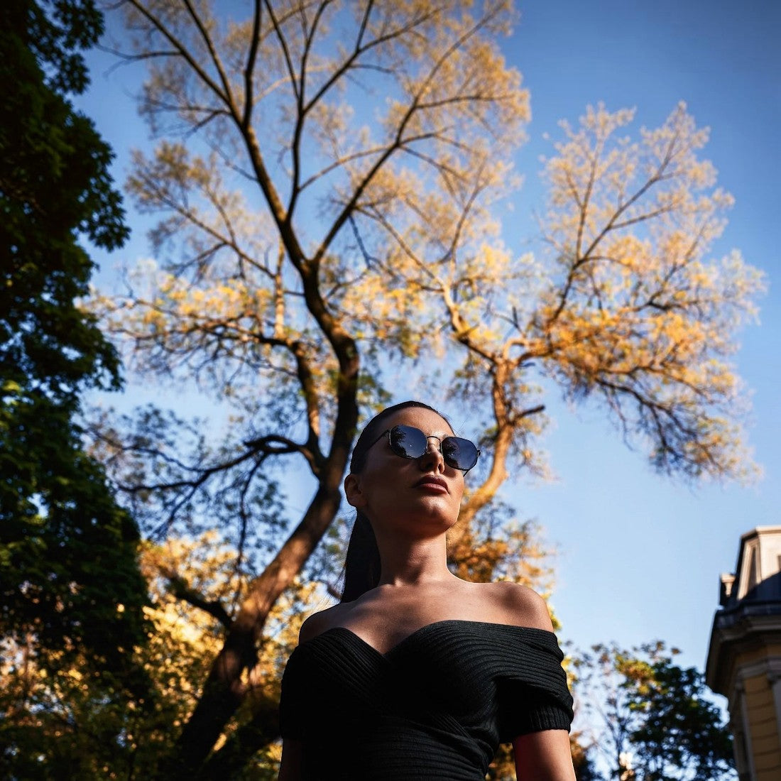 A woman wearing SUL EXTRAS Parade oversized geometric round sunglasses with black frames and smoke lenses outdoors.