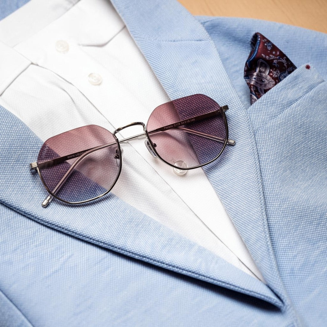 SUL EXTRAS Parade oversized geometric round sunglasses with gradient lenses resting on a light blue blazer and shirt.