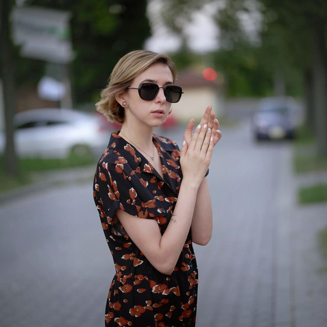 A woman wearing SUL EXTRAS Spark polarized sunglasses with a black frame, styled with a patterned dress outdoors.