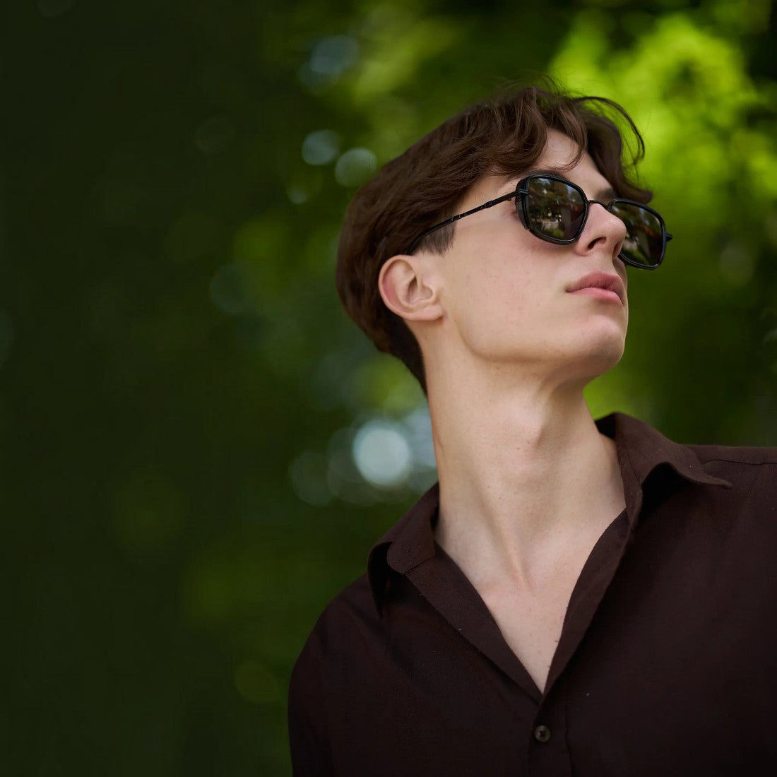 A young man wearing SUL EXTRAS Spark polarized sunglasses with a durable black frame outdoors in a park.