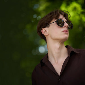 A young man wearing SUL EXTRAS Spark polarized sunglasses with a durable black frame outdoors in a park.