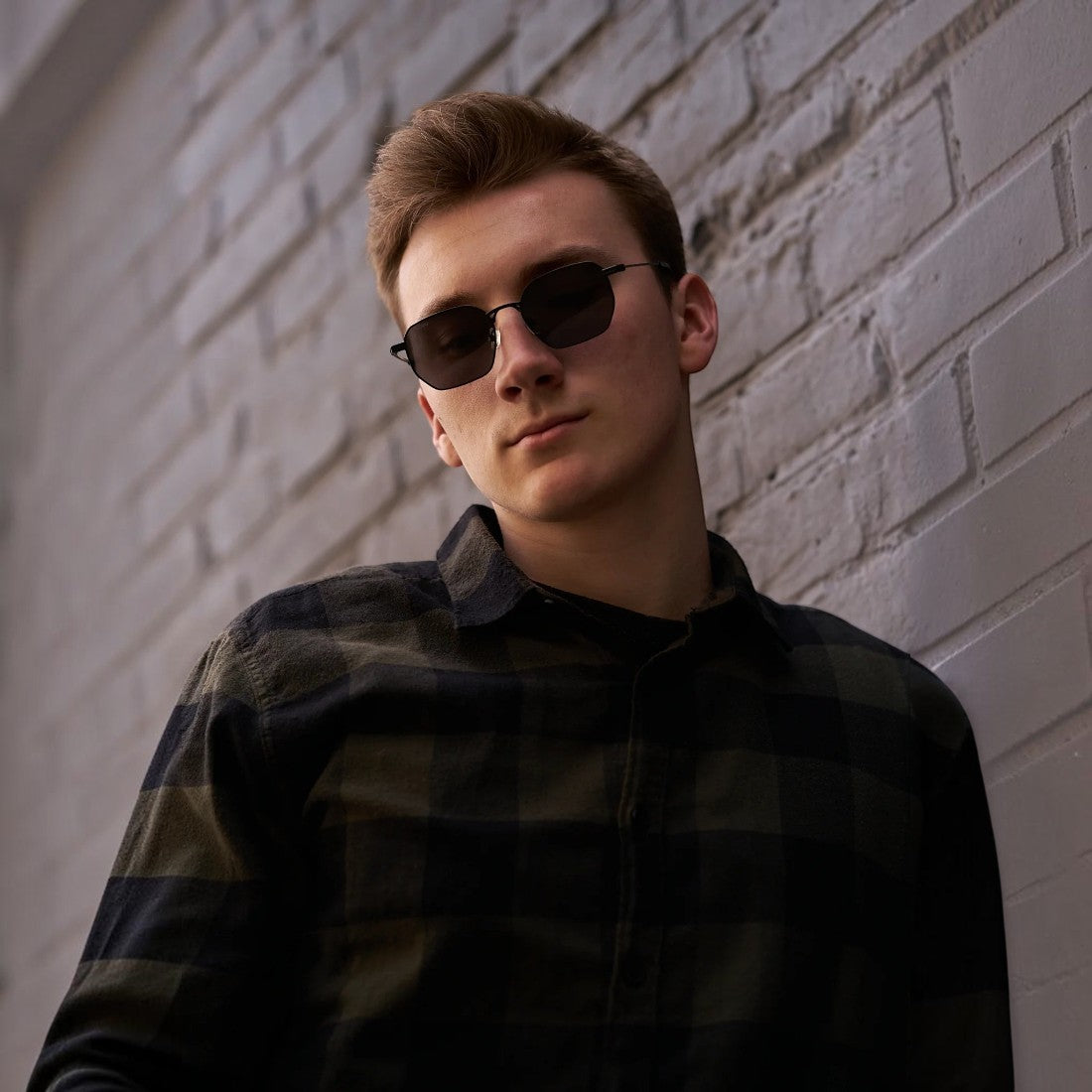 Man wearing SUL EXTRAS Terra angular polarized sunglasses with a lightweight metal and plastic frame against a wall.