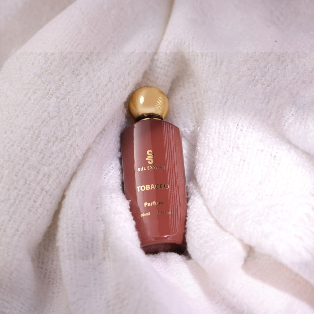 SUL EXTRAS Tobacco Parfum bottle with a gold cap, nestled in a soft white textured fabric.