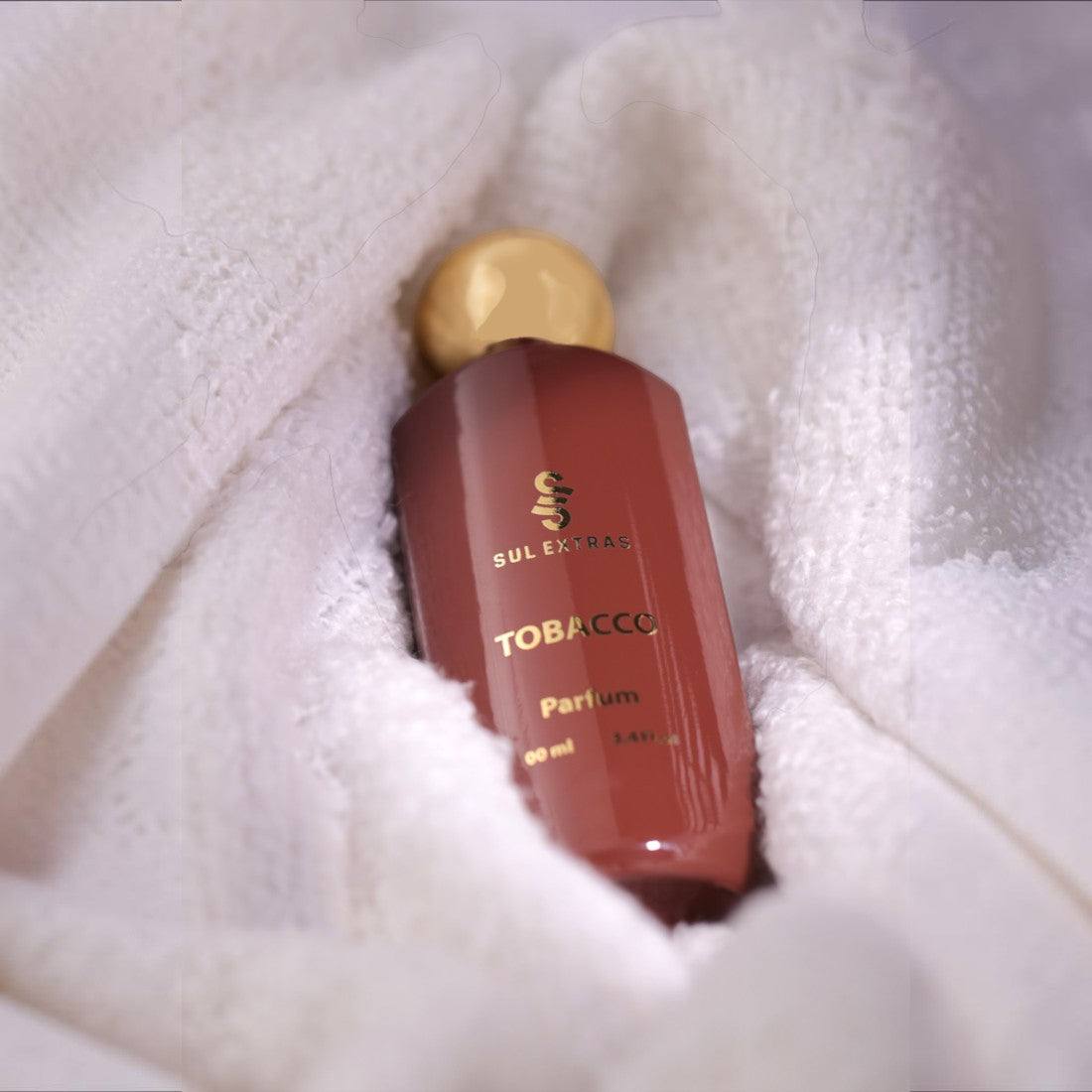 SUL EXTRAS Tobacco Parfum bottle with a gold cap nestled in a soft white textured towel