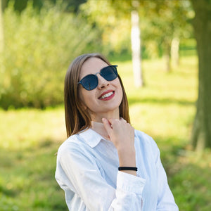 Woman wearing SUL EXTRAS Visi rectangle sunglasses with shiny black frames and green lenses in a park setting
